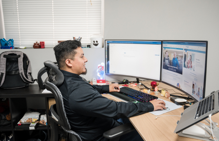 Alejandro sitting at his desk smiling while he works on managing websites